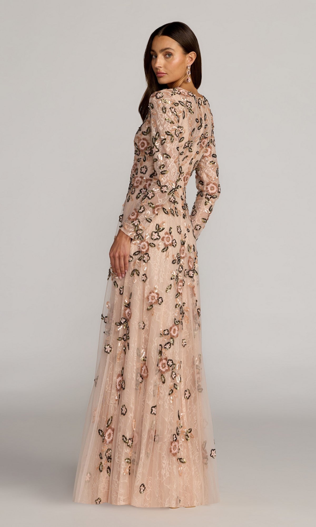 A woman wearing the Mac Duggal 6239 long formal dress in blush, featuring floral embroidery, stands and looks over her shoulder against a plain background. This elegant gown exudes timeless style and modern sophistication.